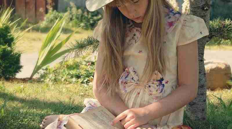 A young girl sits in the grass reading a book demonstrating bibliotherapy.