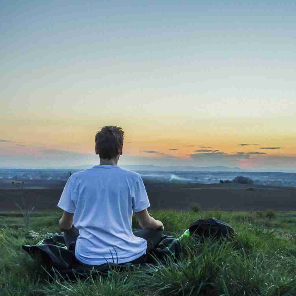 Man sitting in a field at sunset meditating.