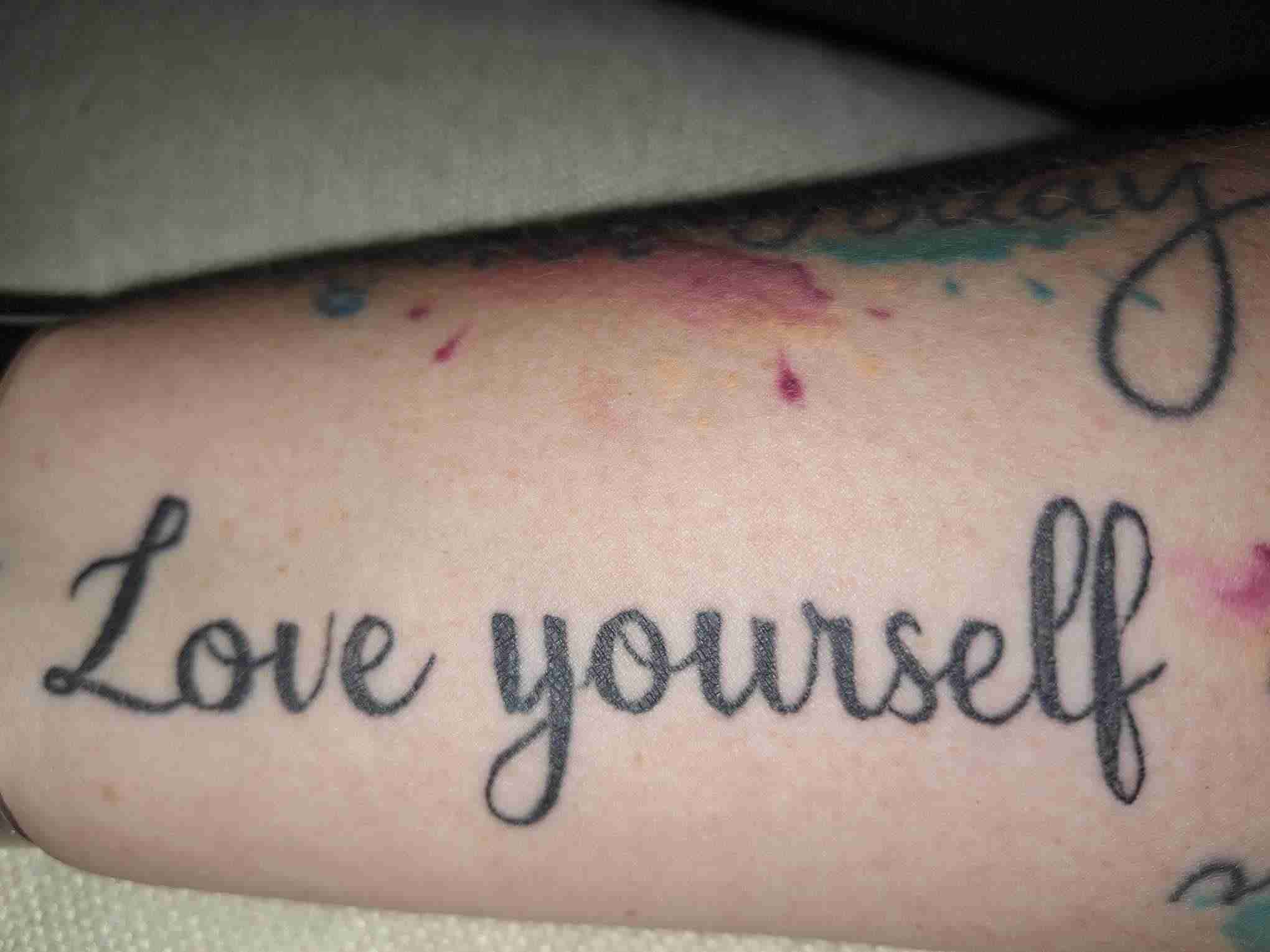 A phot of the author's arm and her tattoo reminding her that "love yourself" is the first step in how to find love.