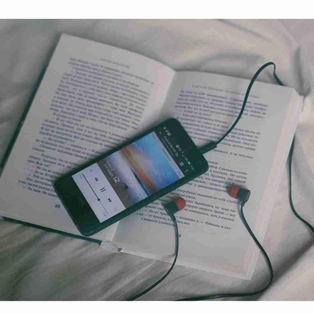 Photo of open book and ipod with headphones attached sitting on bed
