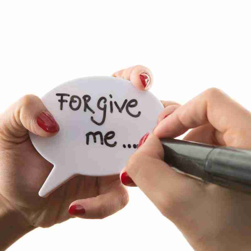 A lady is writing "forgive me" on a little speech bubble with a permanent marker.