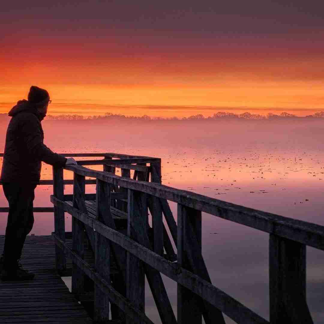 Man standing on a pier at sunrise.