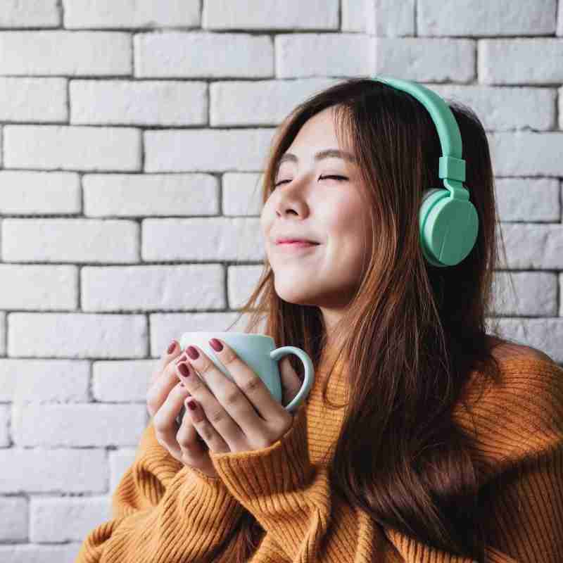 Woman sipping tea with eyes closed and headphones on looking happy and serene