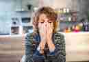A woman sitting at a table with her face in her hands and her eyes closed, demonstrating what it feels like to be with someone who is emotionally unavailable.