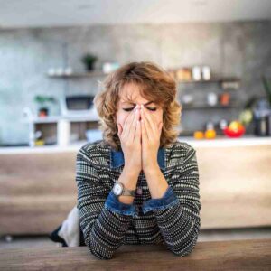 A woman sitting at a table with her face in her hands and her eyes closed, demonstrating what it feels like to be with someone who is emotionally unavailable.