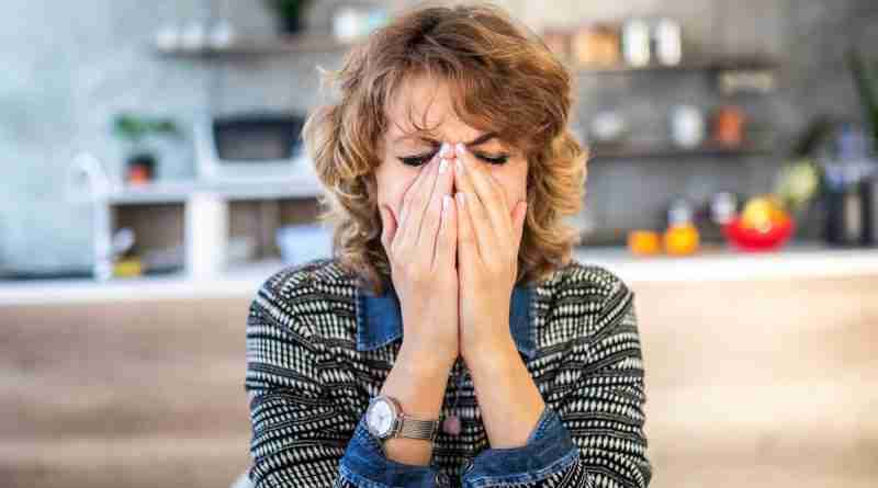 A woman sitting at a table with her face in her hands and her eyes closed, demonstrating what it feels like to be with someone who is emotionally unavailable.