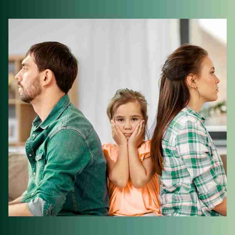 A man and a woman sit with their backs to each other. A little girl sits between them with her face in her hands.