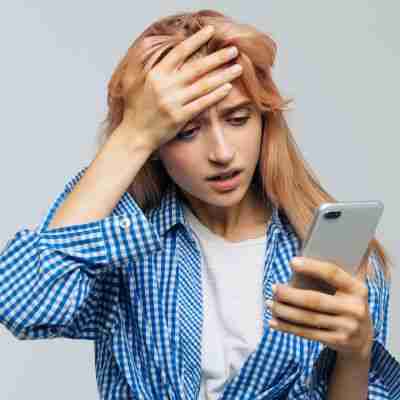 Photo of woman with hand on head looking at phone disappointed and upset to indicate challenges arising