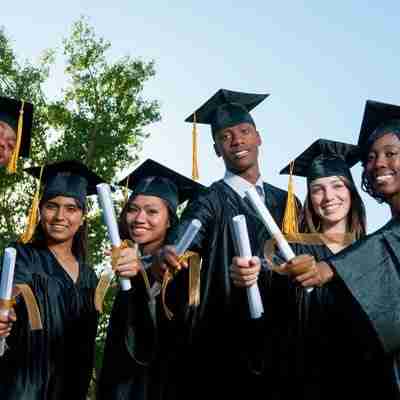 A diverse group of graduates in their caps and gowns, holding their diplomas in front of them.