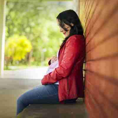 Photo of woman in red leather jacket sitting with hands on pregnant belly