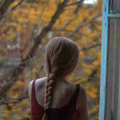 photo of back view of woman with red hair in a braid looking out a window