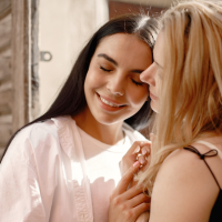 Two women embracing while holding hands in front of them and resting their foreheads on each other's.