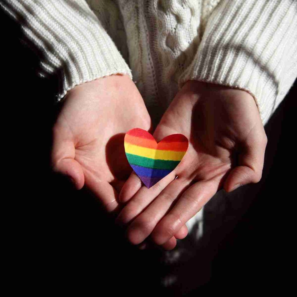 I person holding a rainbow heart offering support to people wondering how to come out.