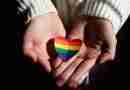 I person holding a rainbow heart offering support to people wondering how to come out.