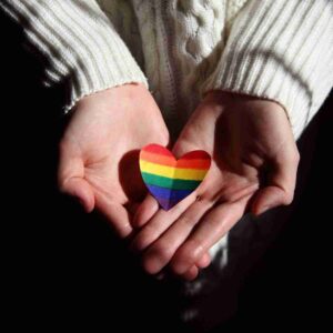 I person holding a rainbow heart offering support to people wondering how to come out.
