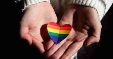 I person holding a rainbow heart offering support to people wondering how to come out.