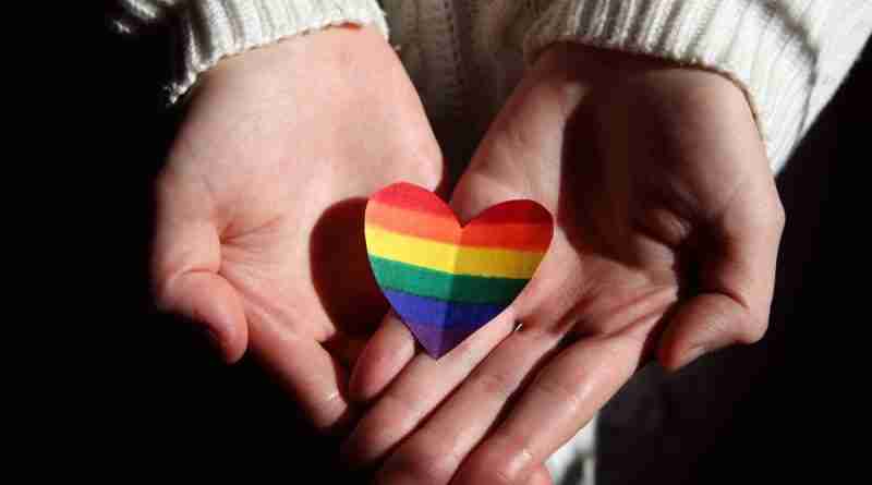 I person holding a rainbow heart offering support to people wondering how to come out.