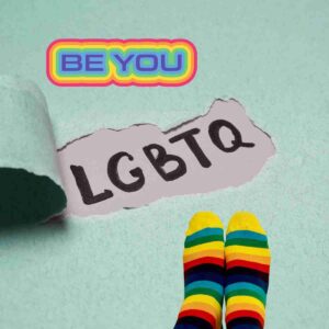A green background with the words "Be You" and "LGBTQ" on it. There are a pair of feet wearing rainbow socks in the corner.