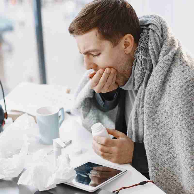 A man wrapped in a blanket and coughing into his hand while suffering from an invisible illness.