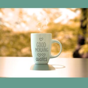 A white coffee cup with the words "Good Morning Quotes" and hearts on a wood table with trees in the background.